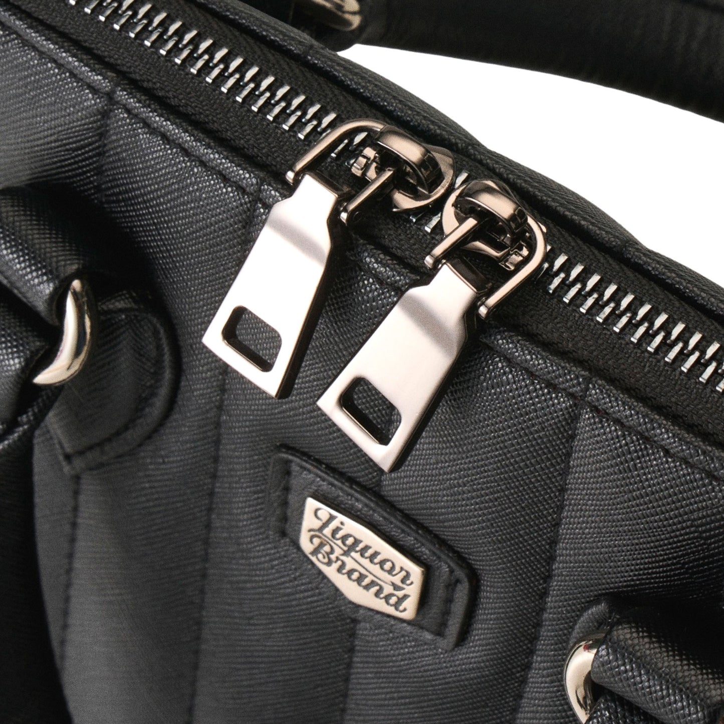 Detalle de la cremallera metálica del bolso Lil' Rocket con doble tirador y el logo de Liquorbrand.