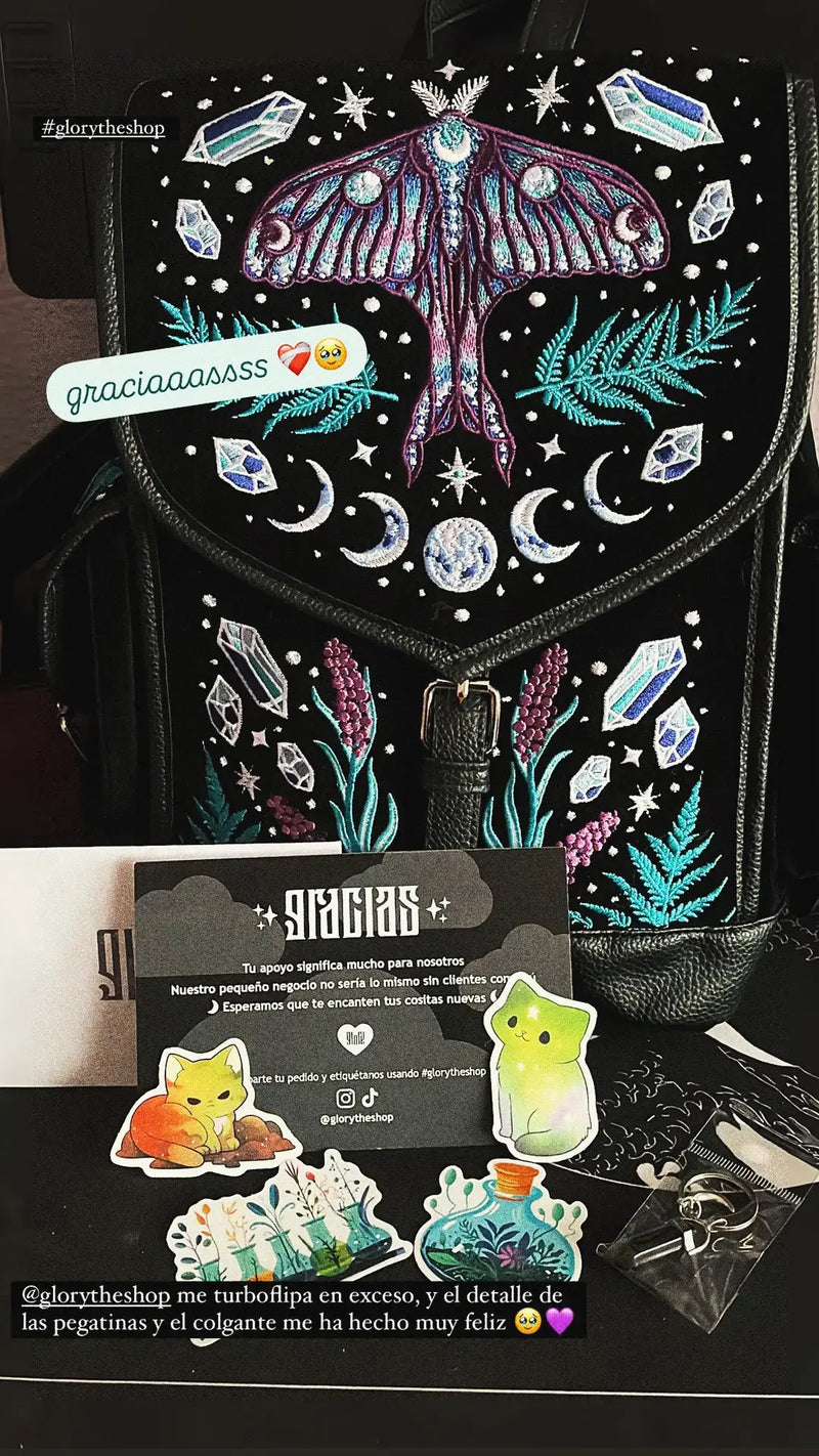 Black backpack featuring detailed embroidery of a moth and moon phases, displayed with stickers and a thank you note.