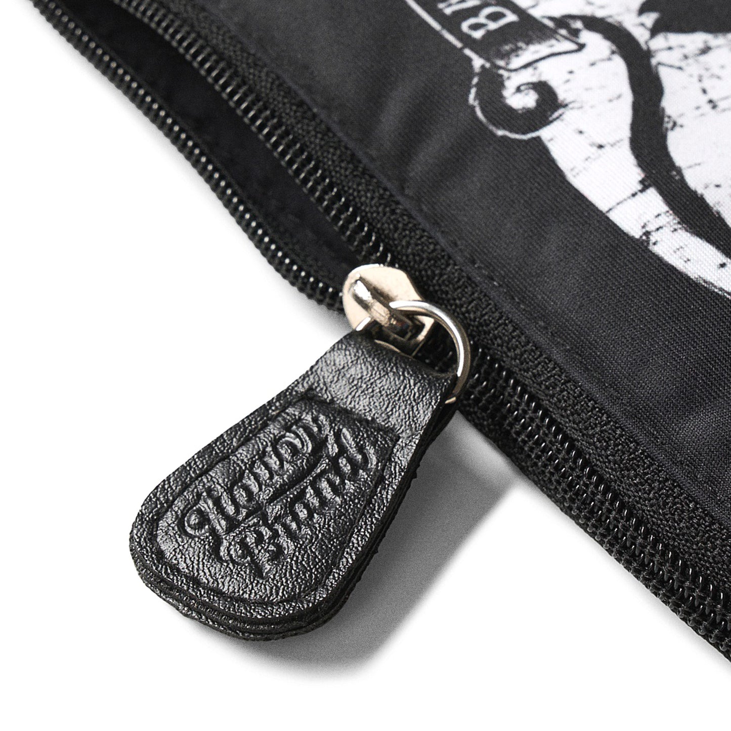 Detalle del tirador de cremallera grabado con el logo de Liquorbrand en cuero negro sobre el neceser Jinx Proof