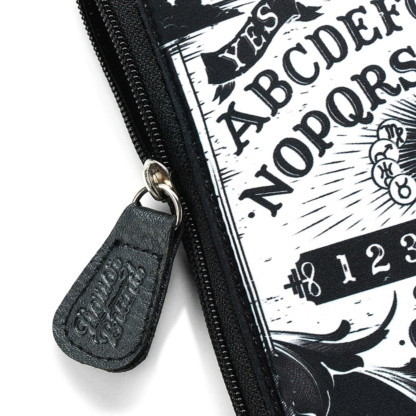 Primer plano del tirador de cremallera de cuero sintético grabado con el logo de Liquorbrand del neceser Ouija.