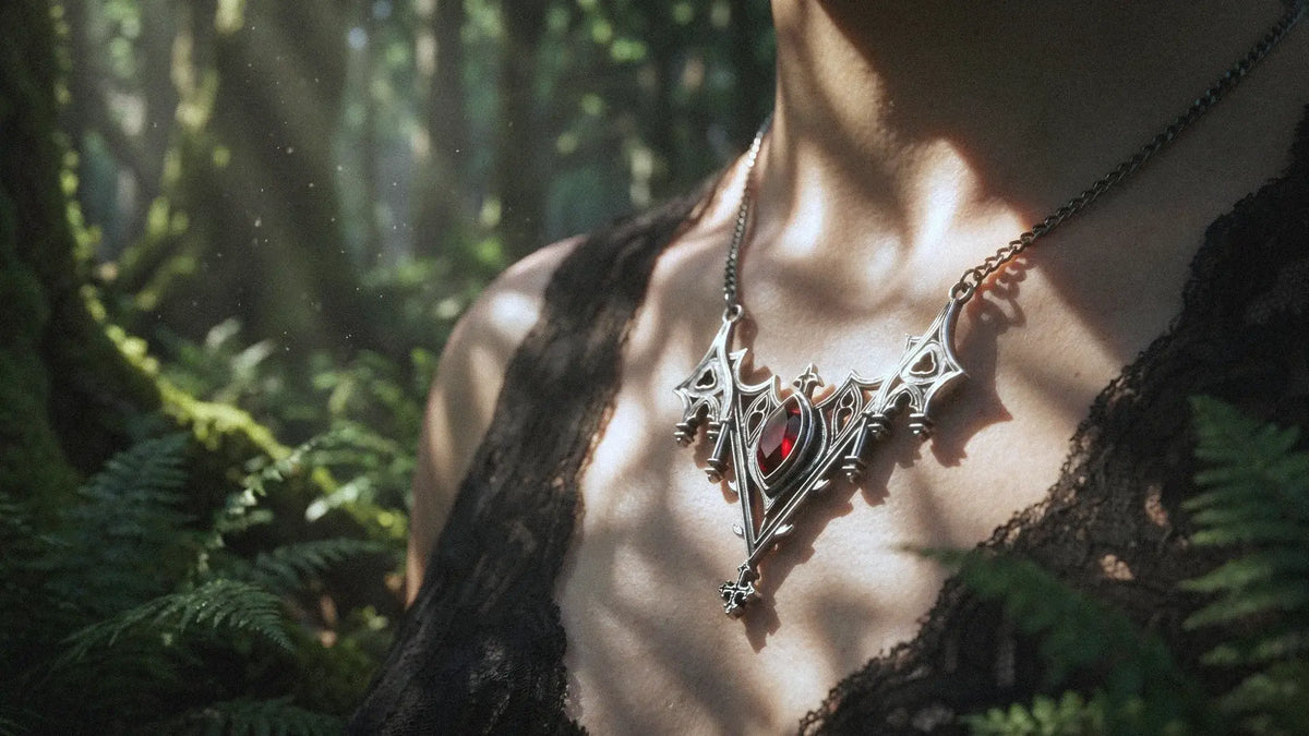 Close-up of a gothic silver cross pendant necklace with a red gemstone, worn over a black lace top, illuminated by dappled sunlight in a lush green forest