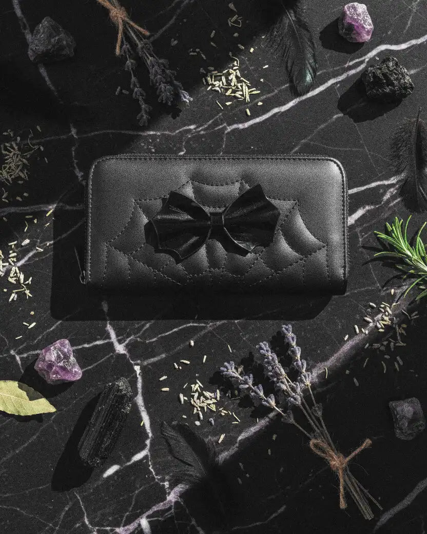 cartera femme fatale de banned alternative apoyada sobre una encimera de mármol con detalles esotéricos al rededor