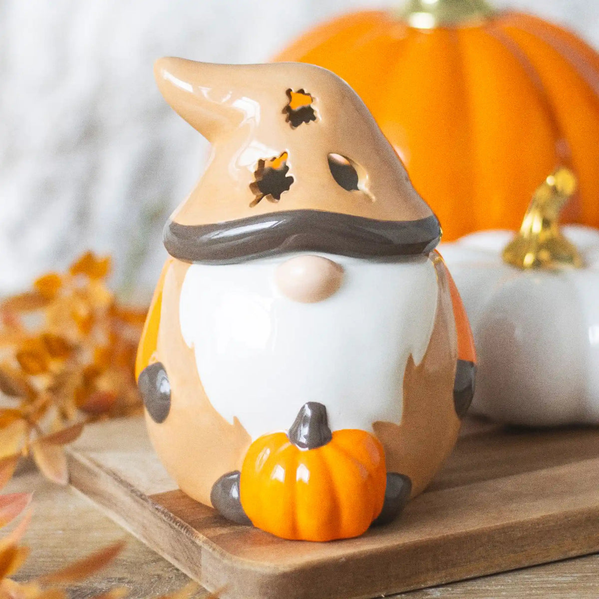 Quemador de aceites esenciales con forma de gnomo adorable otoñal con calabaza y tapa en forma de gorro vista frontal sobre escritorio con decoración al rededor.