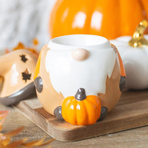 Quemador de aceites esenciales con forma de gnomo adorable otoñal con calabaza y tapa en forma de gorro vista sin tapa en escritorio con decoración al rededor.