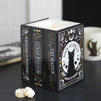 Quemador de aceites esenciales y cera con forma de tres libros de estética witchy con gato en la portada vista sobre escritorio con decoración al rededor.