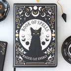 Libreta a5 estilo witchy con diseño de gato negro apoyada sobre una mesa con decoración al rededor.