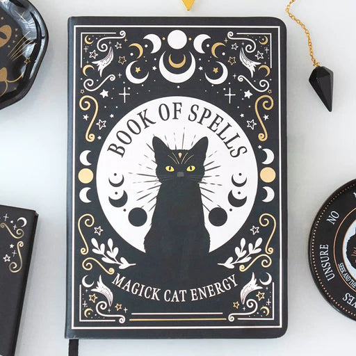 Libreta a5 estilo witchy con diseño de gato negro apoyada sobre una mesa con decoración al rededor.