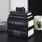 Quemador de aceite y cera con forma de libros apilados y gatito tumbado durmiendo en la parte superior vista en escritorio con decoración al rededor.