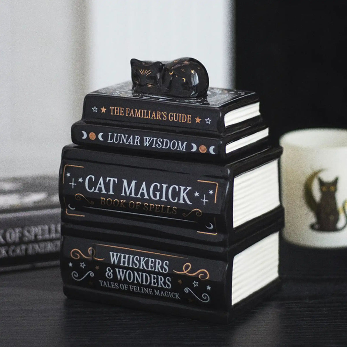 Quemador de aceite y cera con forma de libros apilados y gatito tumbado durmiendo en la parte superior vista en escritorio con decoración al rededor.