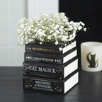 Jarrón con diseño de libros apilados estética witchy y alternativa vista ángulo sobre escritorio con decoración al rededor.