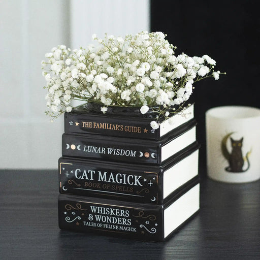 Jarrón con diseño de libros apilados estética witchy y alternativa vista ángulo sobre escritorio con decoración al rededor.