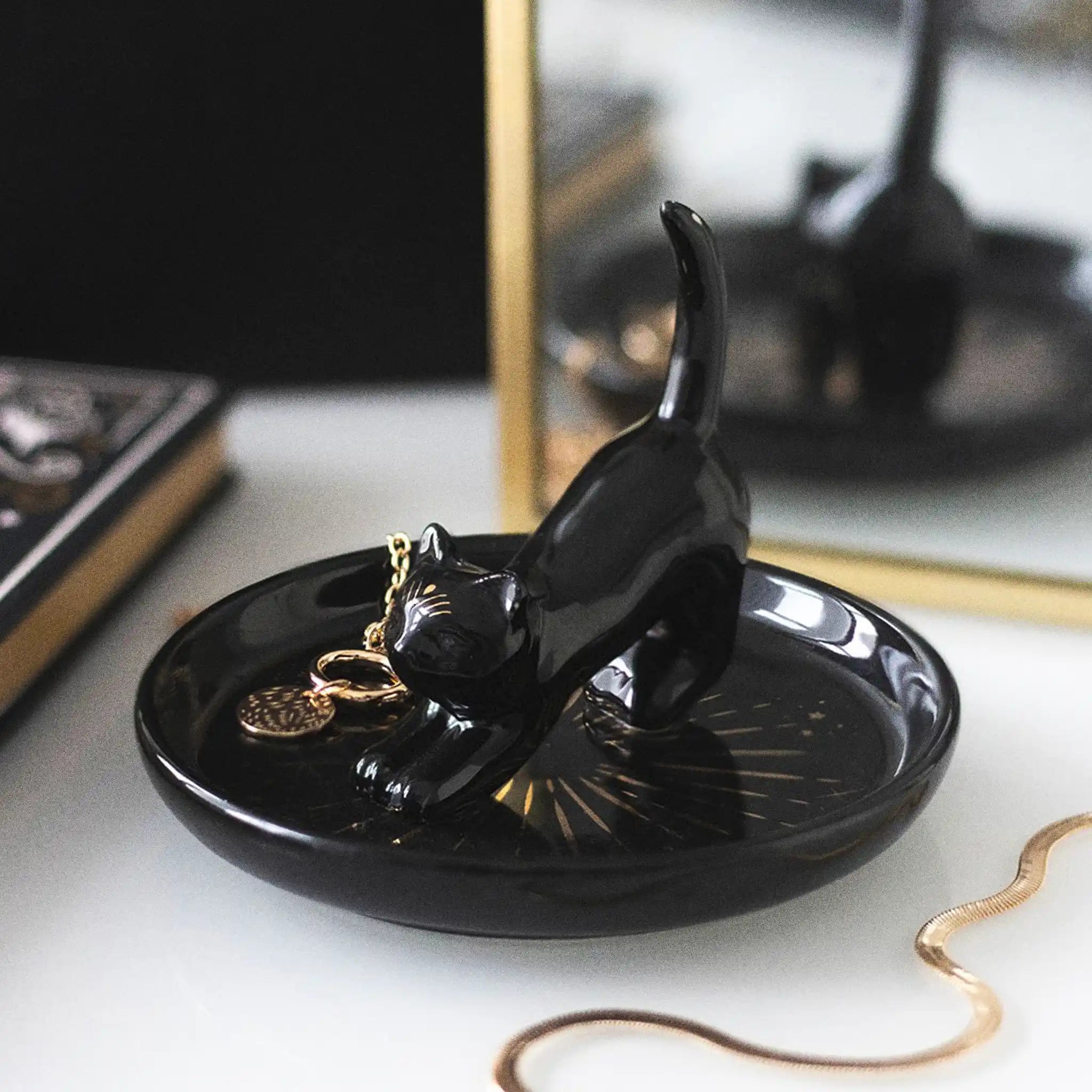 Plato para joyería con gato central con cola hacia arriba para dejar los anillos y joyas visto desde un lateral sobre un escritorio con joyas al rededor.