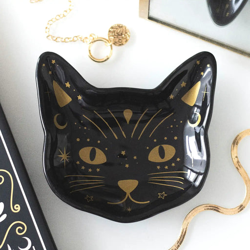 Plato con forma de gato en color negro con detalles en dorado apoyado en una mesa con joyería al rededor.