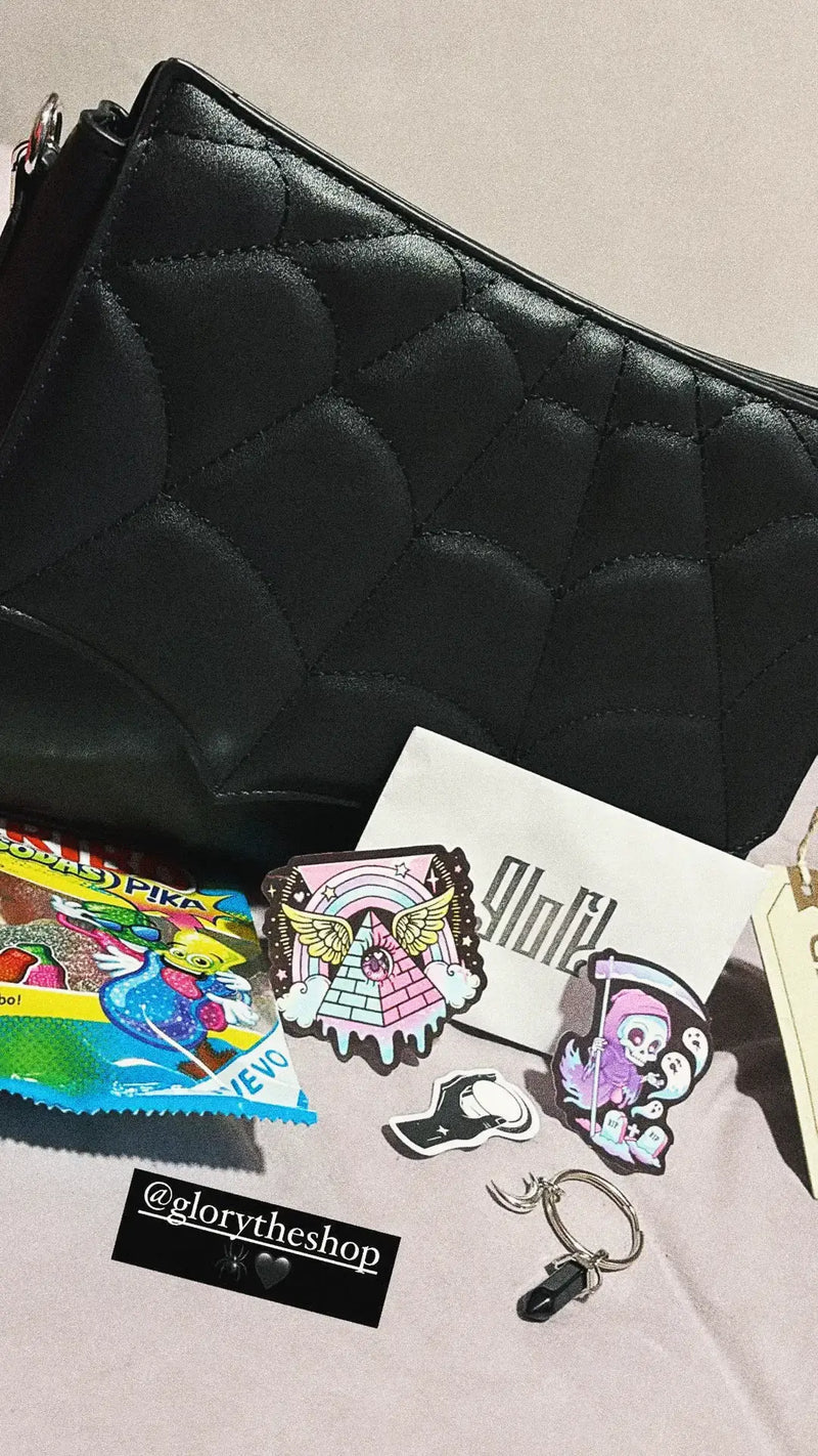 Black gothic handbag with spiderweb stitching displayed with Fini sweets, spooky stickers, and a Glory The Shop logo card.