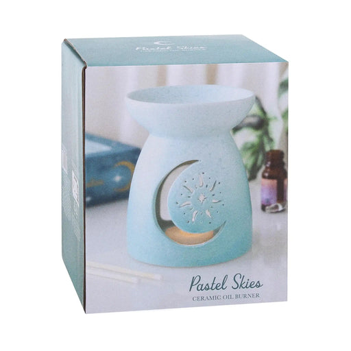 Quemador de aceites esenciales con forma clásica y diseño cut out en la parte frontal de luna y sol y color degradado en tonos azules vista de packaging sobre fondo blanco.