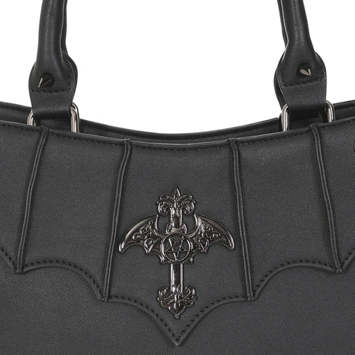 Primer plano del adorno metálico en forma de cruz con alas de murciélago y un pentagrama en el centro.