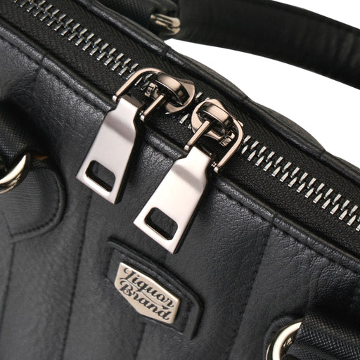 Detalle de la cremallera metálica con doble tirador sobre la parte superior del bolso negro.