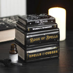 Quemador de aceite y de cera en forma de libros apilados estilo witchy gótico vista sobre escritorio con decoración al rededor.