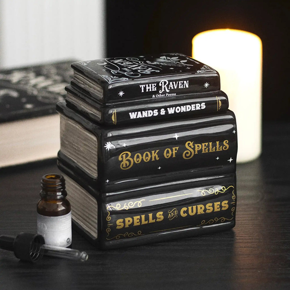 Quemador de aceite y de cera en forma de libros apilados estilo witchy gótico vista sobre escritorio con decoración al rededor.