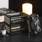 Quemador de aceite y de cera en forma de libros apilados estilo witchy gótico vista sobre escritorio con decoración al rededor y tapa retirada a un lado.