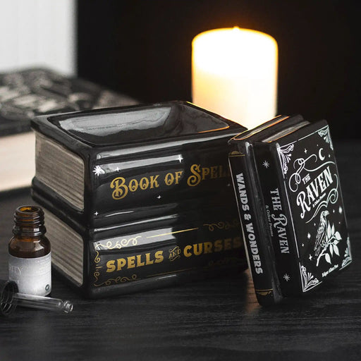 Quemador de aceite y de cera en forma de libros apilados estilo witchy gótico vista sobre escritorio con decoración al rededor y tapa retirada a un lado.