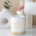 Quemador de aceites esenciales y calentador de cera con diseño de mariposa calada en blanco y base de madera vista frontal sobre escritorio con decoración al rededor.
