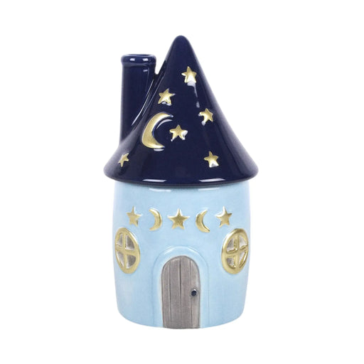 Quemador de aceites esenciales con decoración estilo whimsical y celestial de estrellas y lunas en pequeña cabaña acogedora vista frontal sobre fondo blanco.
