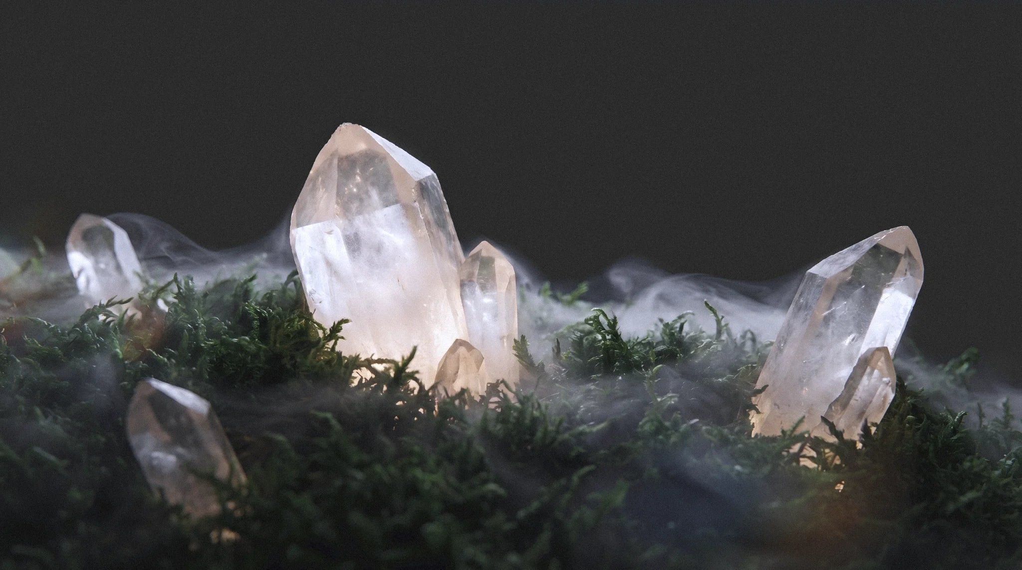 Cluster of glowing clear quartz crystals emerging from green moss with swirling mist, dramatic dark background, extreme macro nature photography