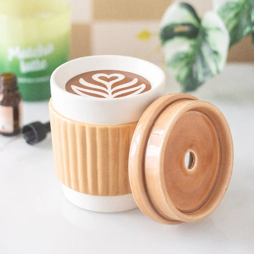 Quemador de aceites esenciales con forma de taza de café take away aesthetic vista fontal con tapa quitada sobre escritorio con decoración alrededor.
