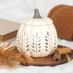 Quemador de aceites esenciales y calentador de cera con diseño en forma de calabaza calada en tonos crema vista frontal sobre escritorio con decoración al rededor.