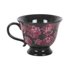 Taza negra de estética dark romance en negro con flores en color púrpura vista de taza y asa sobre fondo blanco.