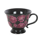 Taza negra de estética dark romance en negro con flores en color púrpura vista de taza y asa sobre fondo blanco.