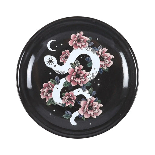 Plato de joyería redondo negro con diseño de serpiente enroscada en flores, estrellas y luna vista desde arriba sobre fondo blanco.