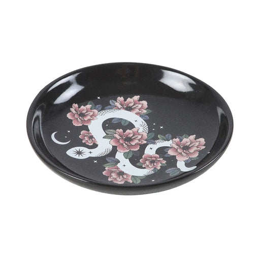 Plato de joyería redondo negro con diseño de serpiente enroscada en flores, estrellas y luna vista desde un lateral con fondo blanco.