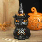 Quemador de aceite en forma de gato negro con gorro de brujo con florecitas y decoración estilo halloween y otoñal vista frontal sobre escritorio con decoración al rededor.