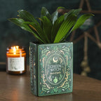 Jarrón verde Green Witchy Book of Spells de cerámica estilo witchy, whimsical y fairycore de cerámica para las amantes de los libros vista frontal encima de escritorio con decoración al rededor.