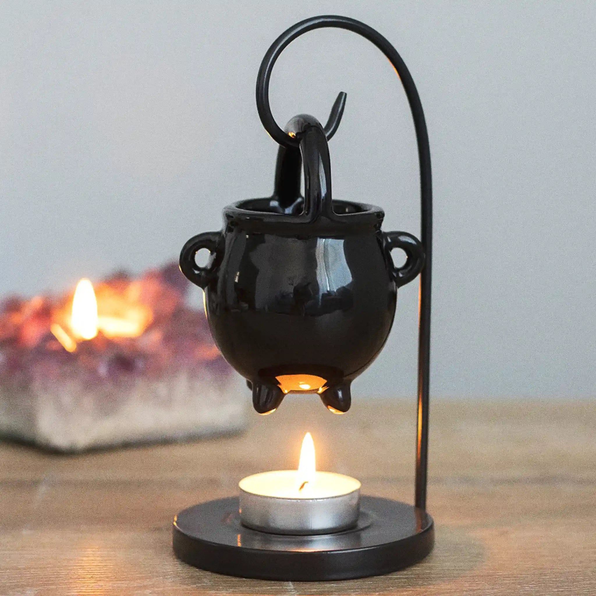 Quemador de aceites esenciales colgante con forma de caldero de bruja estilo witchy gótico vista frontal sobre escritorio con decoración al rededor.