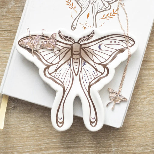 Bandeja para joyería con forma de polilla en blanco con estampado en tonos marrones sobre escritorio con joyería al rededor.