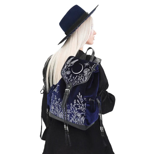 Mochila gótica estilo whimsigoth en tejido de terciopelo combinado con piel sintética con bordados en plateado de luna, flores y estrellas y borlas decorativas vista en hombro de modelo