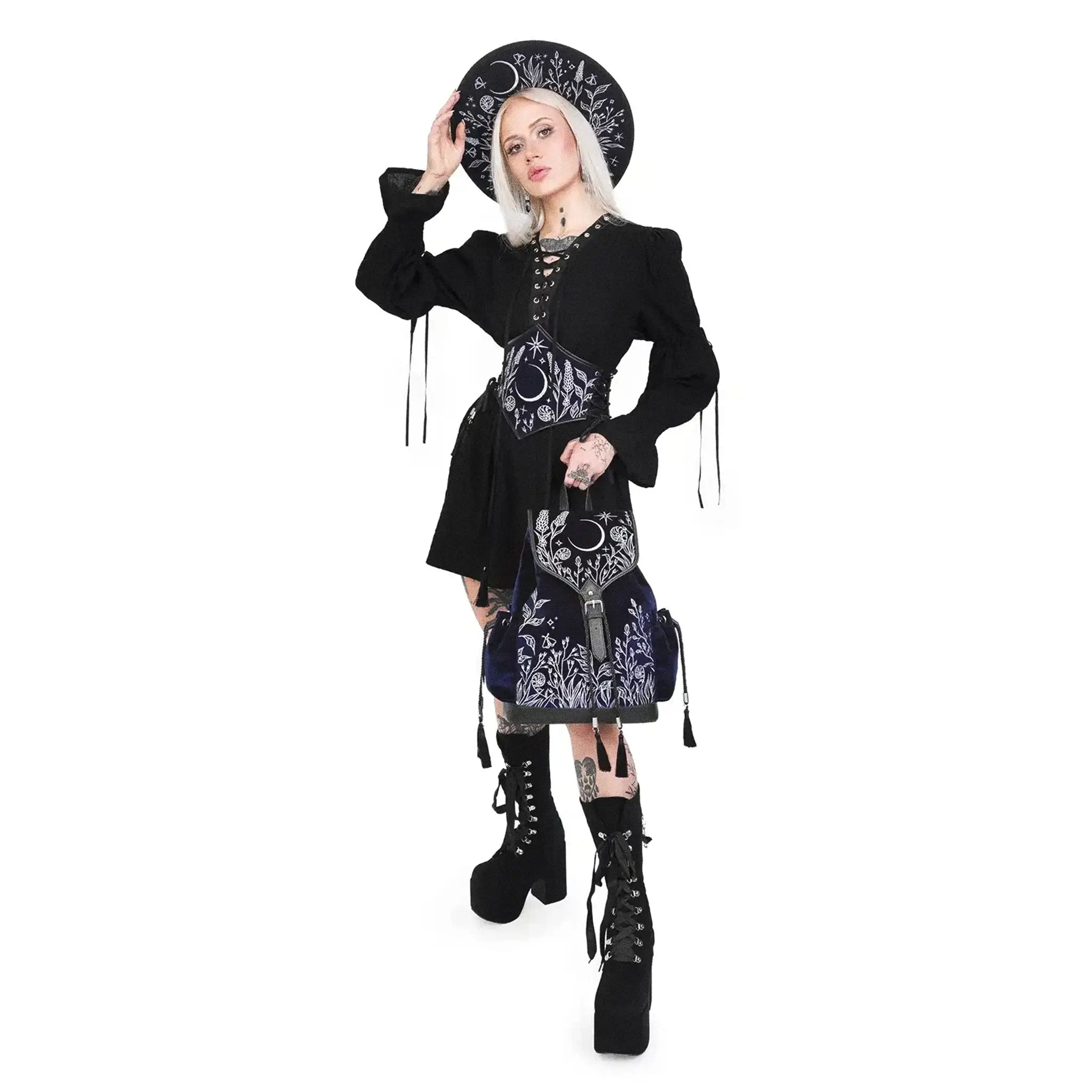 Mochila gótica estilo whimsigoth en tejido de terciopelo combinado con piel sintética con bordados en plateado de luna, flores y estrellas y borlas decorativas vista con modelo de pie