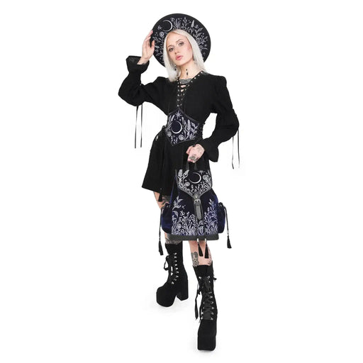 Mochila gótica estilo whimsigoth en tejido de terciopelo combinado con piel sintética con bordados en plateado de luna, flores y estrellas y borlas decorativas vista con modelo de pie