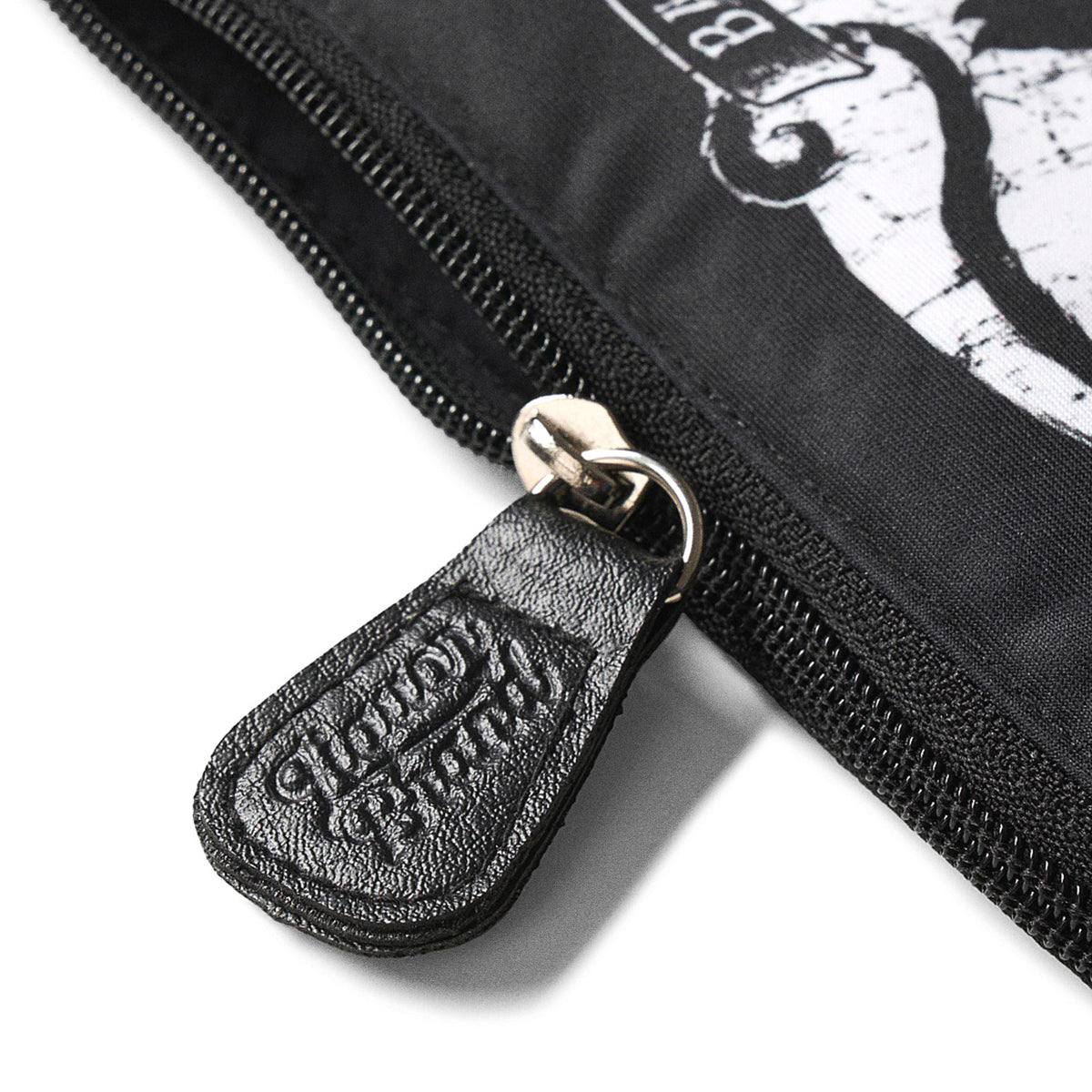 Detalle del tirador de cremallera grabado con el logo de Liquorbrand en cuero negro sobre el neceser Jinx Proof