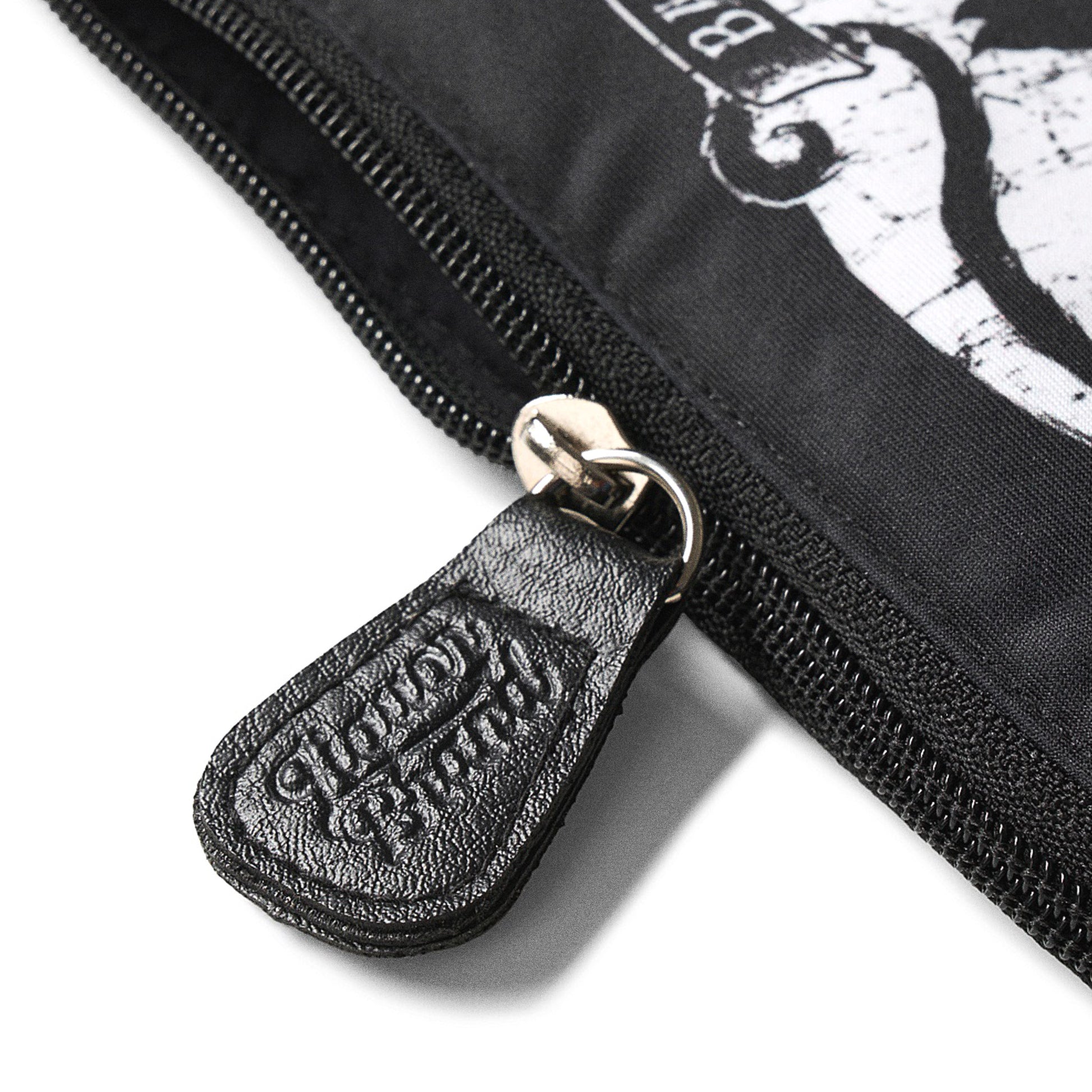 Detalle del tirador de cremallera grabado con el logo de Liquorbrand en cuero negro sobre el neceser Jinx Proof