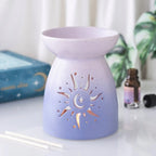 Quemador de aceite con forma clásica en color morado degradado y cut out en forma de sol estilo hippy vista frontal sobre escritorio con decoración al rededor.