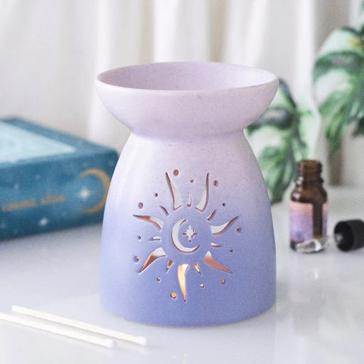 Quemador de aceite con forma clásica en color morado degradado y cut out en forma de sol estilo hippy vista frontal sobre escritorio con decoración al rededor.