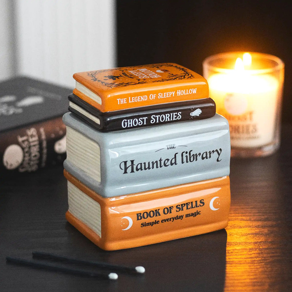 Quemador de aceite y calentador de ceras aromáticas en forma de libros apilados de estética de Halloween y Spooky en naranja, negro y gris vista ángulo sobre escritorio con decoración al rededor.