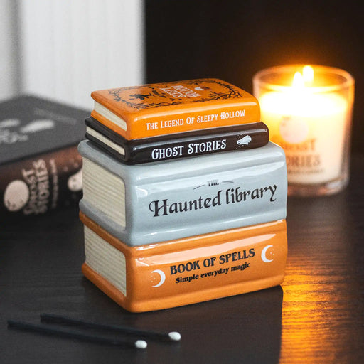 Quemador de aceite y calentador de ceras aromáticas en forma de libros apilados de estética de Halloween y Spooky en naranja, negro y gris vista ángulo sobre escritorio con decoración al rededor.