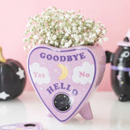 Jarrón estilo pastel goth con diseño de planchette de ouija en rosa estilo kawaii vista ángulo sobre escritorio con decoración al rededor.