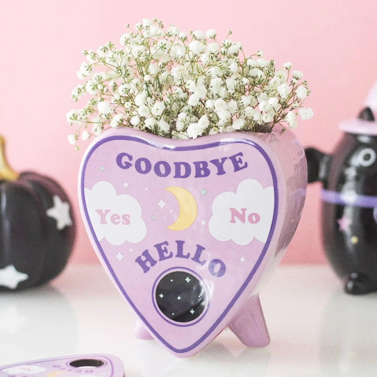 Jarrón estilo pastel goth con diseño de planchette de ouija en rosa estilo kawaii vista ángulo sobre escritorio con decoración al rededor.
