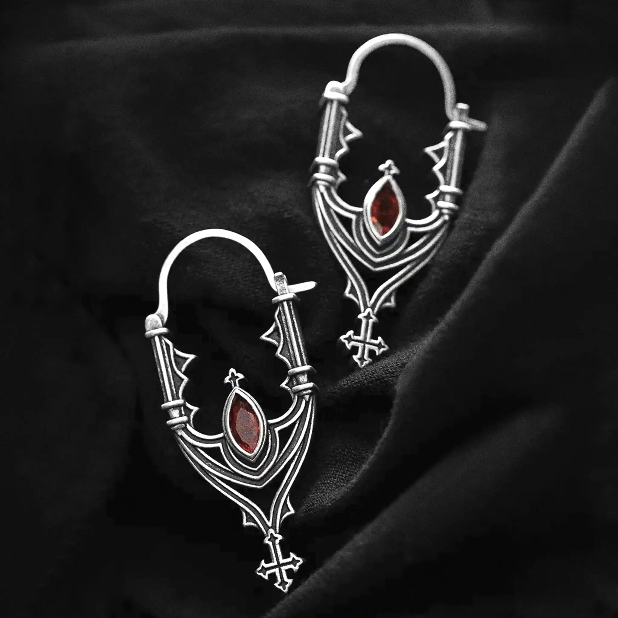 Pendientes inspirados en las catedrales góticas con cruces y piedra roja central estilo whimsigoth fabricado en latón y plata de Restlye vista sobre fondo negro